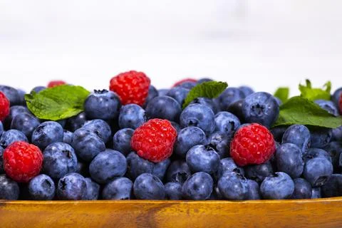 Blueberry and Raspberry With a Green Mint leaf in a Wooden Bowl on a white Stock Photos