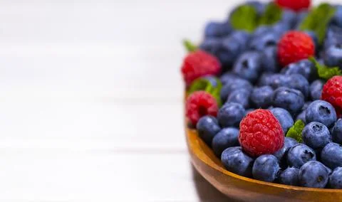Blueberry and Raspberry With a Green Mint leaf in a Wooden Bowl on a white Stock Photos