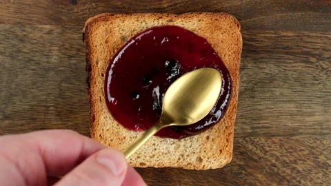 Blueberry jam spreading on bread with a golden spoon, top view Video stock 233971375