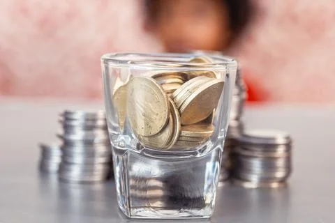 Blur of Children Sitting in Back of Stack of Coins and glass of coins Stock Photos