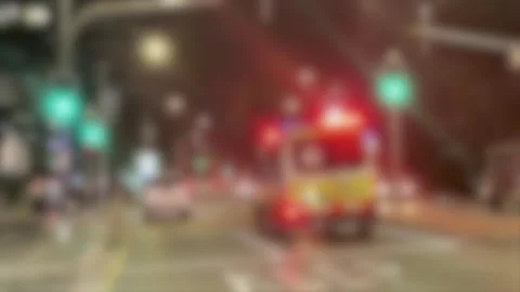 Blurred Ambulance with Flashing Lights Speeding Through City Street at Night Stock Footage 328063933