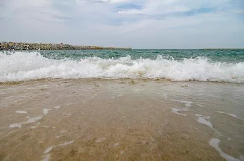 Blurred and selective focus image of wave hitting the beach over cloudy and b Stock Photos