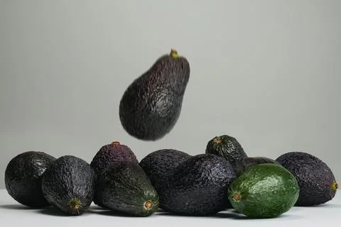 Blurred avocado falling toward group of avocados on gray background Stock Photos