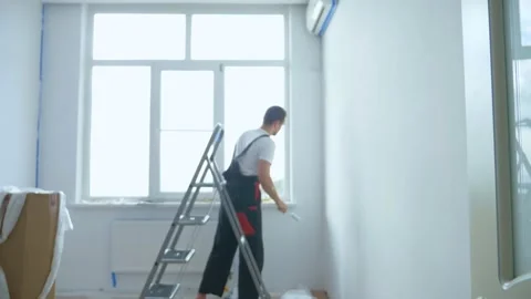 Blurred background. a man on a stepladder paints the walls in the room white Stock Footage 144134598