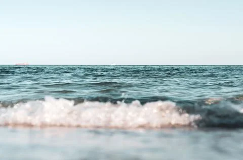 Blurred background, small waves on coast, ships on horizon, bright blue sky,  Stock Photos