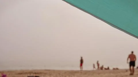 Blurred beachgoers behind an umbrella create a soft summer leisure concept Stock Photos