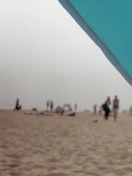 Blurred beachgoers behind an umbrella create a soft summer leisure concept Stock Photos
