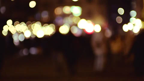 Blurred city lights create a vibrant bokeh effect as people walk by at night.  Stock Footage 326153526