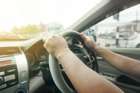 Blurred close up of hands on steering wheel in sunny day traffic jam, driving Stock Photos