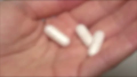 Blurred, closeup of taking or holding 3 white medical capsules in hand. 4K Stock Footage 256621781