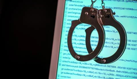 Blurred computer screen with program code visible, and shaking handcuffs Foto stock