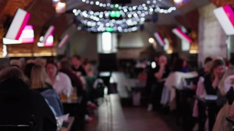Blurred crowd relaxing inside busy restaurant bar with warm string lights, soft Stock Footage 337648353