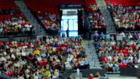 Blurred crowd sitting in stadium stands during large public event with shallow Stock Footage 345480399