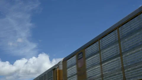 A blurred freight train moving under a blue sky that has white puffy cumulus Stock Footage 336807524