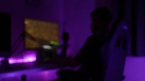 Blurred gamer at desktop computer with purple neon lighting, static shot for Stock Footage 344321168