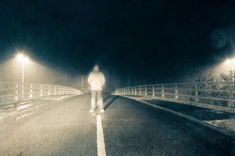 A blurred hooded figure standing in the middle of the road on a winters night Stock Photos