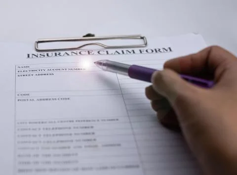 Blurred human hand using pen point to Insurance claim form,Lens flare effect, Stock Photos