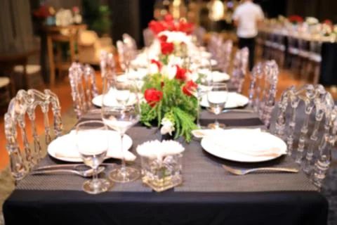 A blurred image of a dinner table with red roses. And green decorative leaves Stock Photos