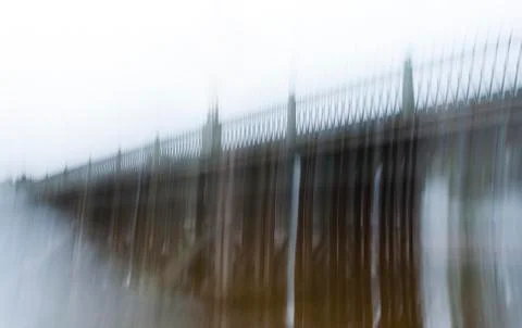 Blurred image of a long ancient bridge with a wrought-iron fence in the fog Stock Photos