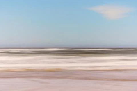 Blurred image of ocean waves under a clear sky with a faint cloud. Stock Photos