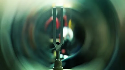 A Blurred Man and a Tuning Fork with Vibrating Audio Waves in a Room. Close Up. Stock Footage