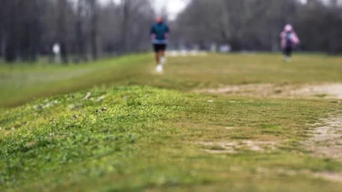 Blurred Man Jogging in Park - Focus on Green Grass Foreground Stock Footage 330489706