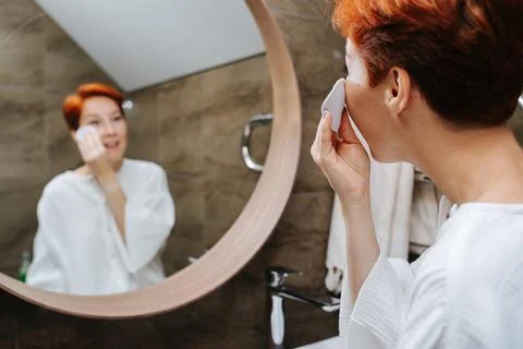 Blurred mirror image of a short-haired mature woman applying lotion on her fa Stock Photos