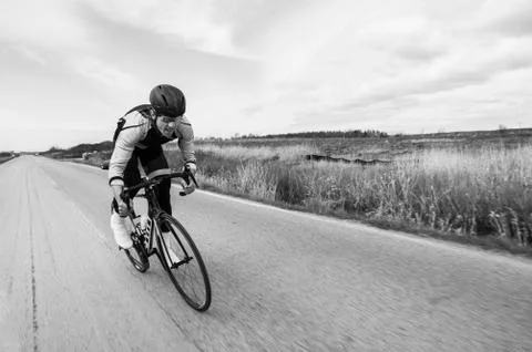 Blurred motion of cyclist riding bicycle on country road by field against sky Stock Photos