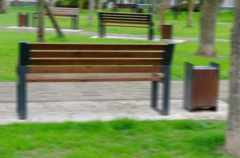 Blurred motion, defocus. Wet empty park bench against the backdrop of a green Stock Photos