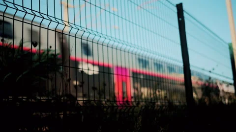 Blurred motion of a modern train seen through a wire fence with blue sky Stock Footage 320592224