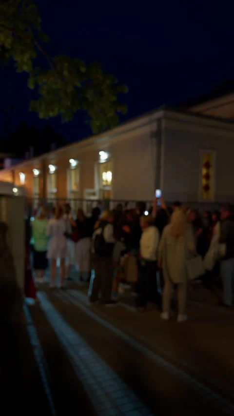 Blurred night crowd gathered outside illuminated building with glowing windows Video stock 345605530