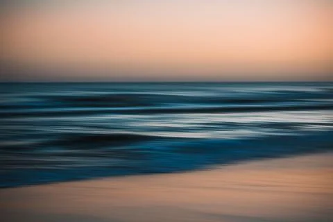 Blurred ocean waves under a soft orange and blue sky at dusk. Stock-Fotos