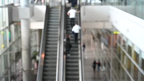 Blurred out of focus tracking shot of people using escalators in an airport mall Stock Footage 154870311