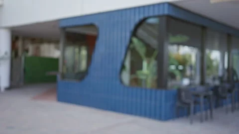 Blurred outdoor cafe with blue wall and glass windows, featuring defocused .. Stock Footage 284281058
