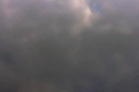 Blurred reflection of clouds on the surface of the water with light ripples. Stock Photos