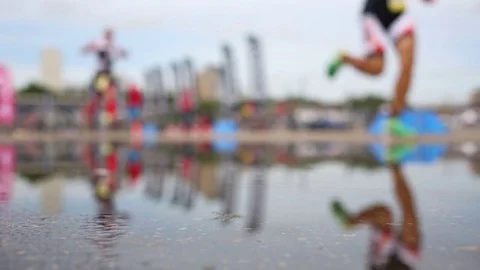 Blurred runners go the distance and reflected on the surface of puddle Stock Footage 73727352