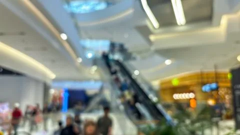 Blurred shoppers move through a bright modern mall with an indoor escalator. Stock Photos