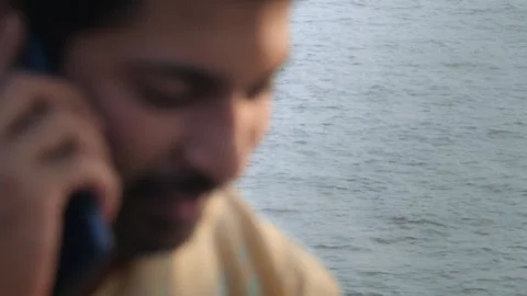 A blurred shot of a man talking on a mobile phone with ocean waves in the back  Stock Footage 325718862