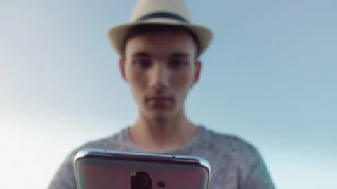 Blurred silhouette of a guy in a hat against a blue sky with a mobile phone in Stock Footage 165704128