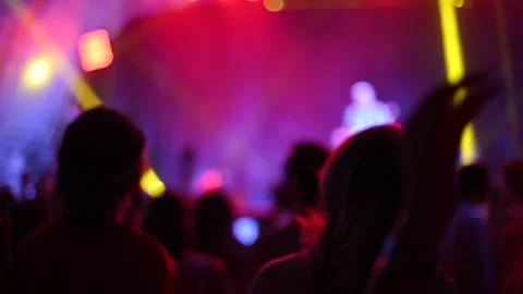 Blurred silhouettes of people raise hands in front of colorful lights in concert Stock Footage 245326487