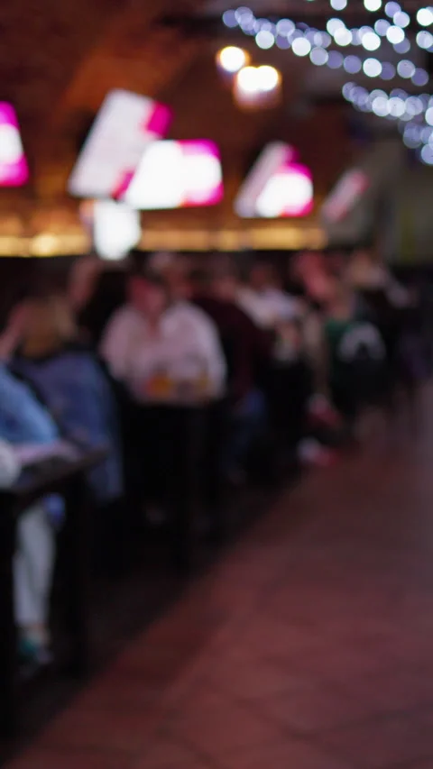 Blurred social gathering inside dim bar interior with seated guests, glowing Stock Footage 337648416