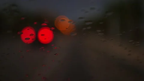 Blurred traffic lights through a windshield with rain droplets at night 스톡 동영상 164609341