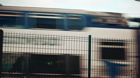 Blurred train passing behind a metal fence, creating an abstract transportation Stock Footage 322944873