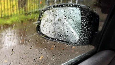 Blurred view from inside a car showing a side mirror covered in heavy raindrops Stock Photos