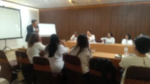 A blurred view of A male presenter is addressing an audience seated at tables in Stock Footage 340533819