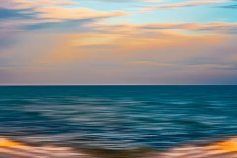 Blurred view of the ocean at sunset with soft waves and colorful sky. Stock Photos