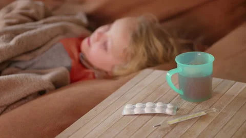 Blurred view of sick child lying on the sofa, hot drink, pills and thermometer Stock Footage 229868525