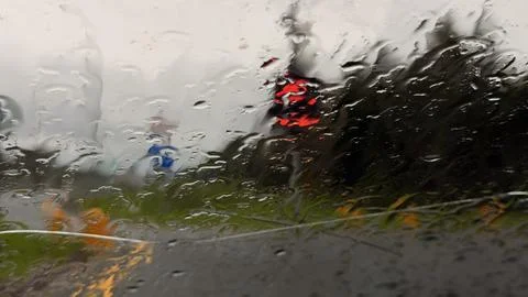 Blurred view through a wet car windshield with heavy raindrops, showing a Stock Photos