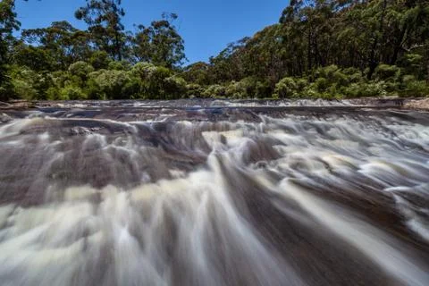Blurred water flow through rapids on a river in a forest Foto stock