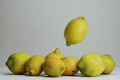 Blurred yellow lemon falling toward other lemons on surface against gray Stock Photos